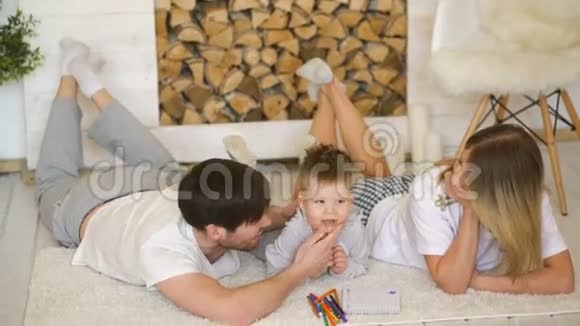 一个带着小儿子的年轻家庭在地板上玩耍在客厅里微笑着亲吻他视频的预览图