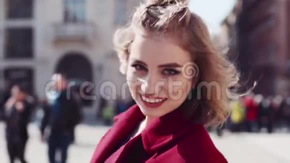 年轻的女人穿着一件红色的外套红唇沿着街道走有着嬉戏的心情戏弄着相机阳光明媚视频的预览图