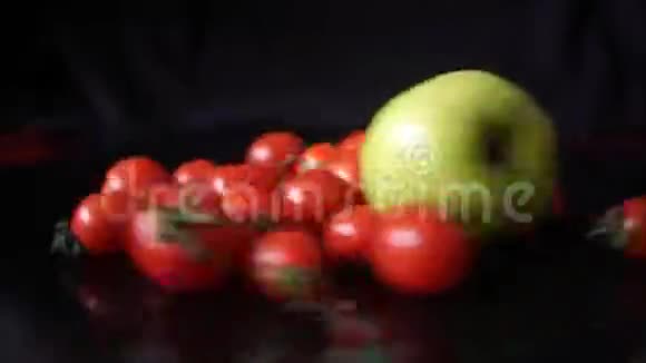 红樱桃西红柿和绿苹果在黑色背景上快速旋转视频的预览图