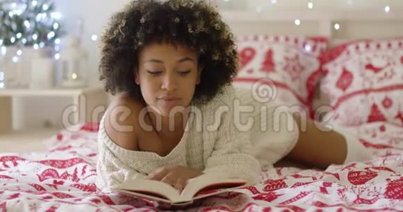 平静美丽的非洲女人躺在床上看书视频的预览图