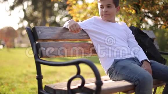 穿白色毛衣的少年坐在长凳上带背包的帅哥学校男孩视频的预览图