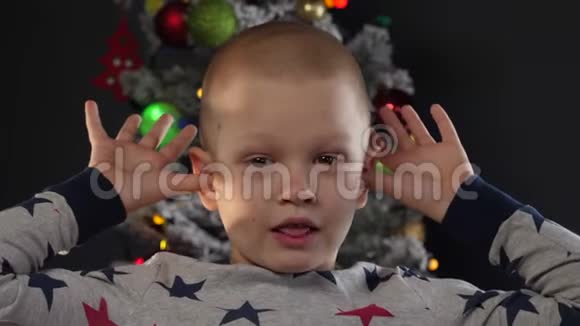 快乐的孩子在圣诞树前的花环和绿色的不明飞行物火球发光的球体闪烁的灯光上展示着鬼脸视频的预览图