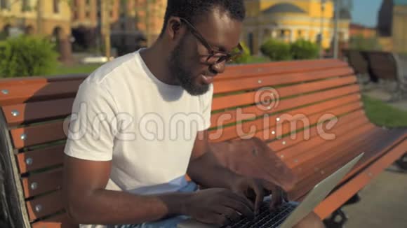 一个微笑的男人在公园里用笔记本电脑打字视频的预览图