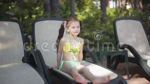 一个穿黄色泳衣的小女孩正坐在日光浴床上晒太阳视频的预览图