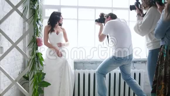 摄影师拍摄一个美丽的黑发新娘模特在大师班的婚纱里女孩在摆姿势视频的预览图