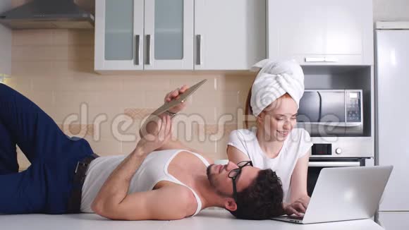 年轻的商务夫妇在家厨房里用笔记本电脑工作家商业的概念自由职业视频的预览图