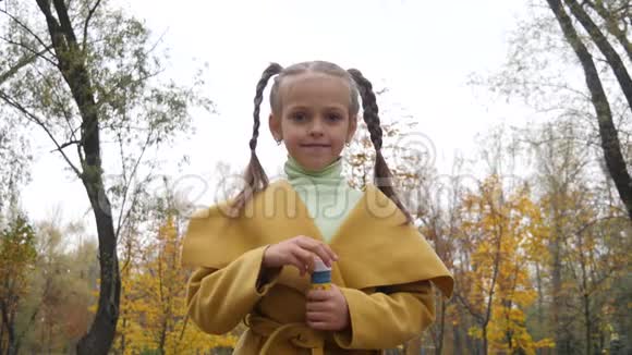 阴天时穿着黄色外套的小女孩在公园里吹气泡视频的预览图