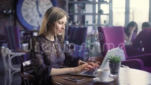 可爱的女人在咖啡馆里带着笔记本电脑漂亮的女人带着一杯咖啡坐在咖啡馆里用笔记本电脑视频的预览图
