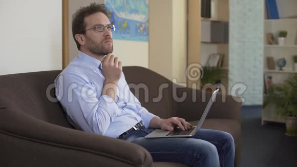 坐在沙发上用笔记本电脑思考新文章的男记者视频的预览图