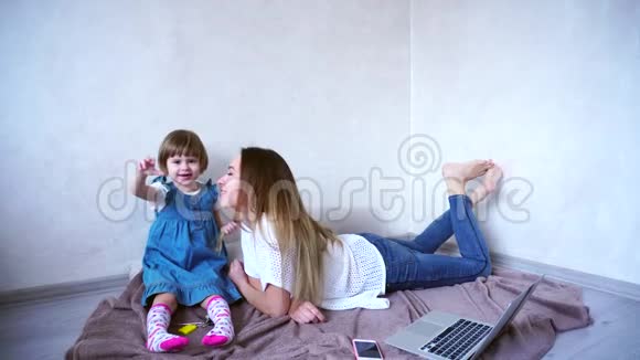 可爱的女孩美丽的母亲和宝贝女孩放纵和摆在相机上在明亮的房间里坐在地板上玩视频的预览图