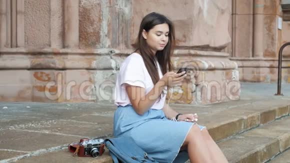 4k段美丽的黑发女孩坐在街上在智能手机上听音乐视频的预览图