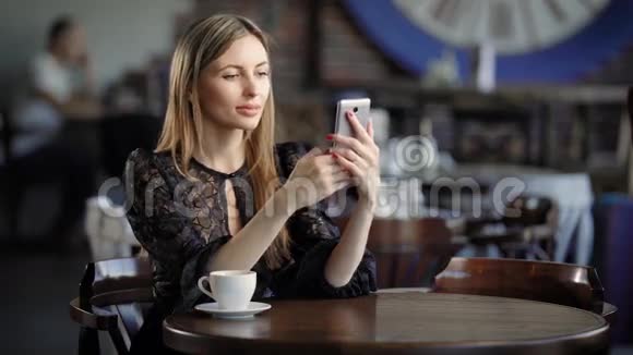 微笑的女孩自拍年轻的微笑女性优雅的裙子坐在咖啡馆的桌子上自拍视频的预览图