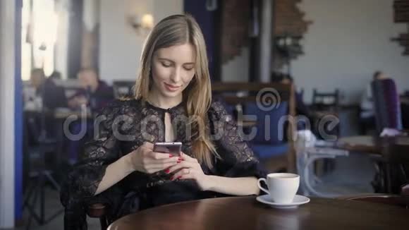 微笑的女人用电话年轻优雅的女孩坐在咖啡馆的桌子上使用智能手机视频的预览图