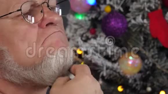 快乐的老人在花环上的圣诞树背景上用梳子梳理他的灰色胡须绿色的UFO球质子紫色玩具视频的预览图