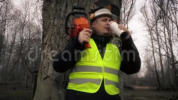肩膀上有电锯的工人在树旁喝咖啡视频的预览图