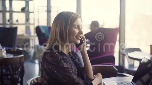 美丽的微笑的女性在说话年轻的微笑的女性穿着优雅的裙子坐在咖啡馆里打电话视频的预览图