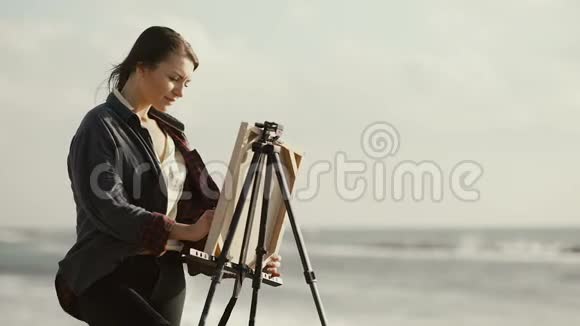 那个黑发女人在海滩上画架上画画视频的预览图