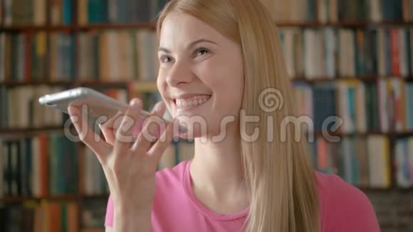 快乐的微笑学生站在图书馆用她的智能手机和朋友笑着聊天视频的预览图