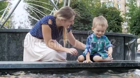 与妈妈一起在公园的喷泉中玩耍和泼水的可爱活泼的幼儿男孩慢动作视频视频的预览图