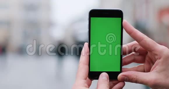 男人手里拿着一部智能手机手里拿着绿色屏幕站在街上视频的预览图