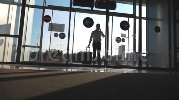 年轻的商人带着行李去机场打电话带着手提箱走路的人一个家伙视频的预览图