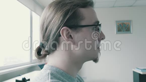 一个戴眼镜的年轻人的肖像他的头发被绑在尾巴上这位年轻的职员正在办公室工作视频的预览图
