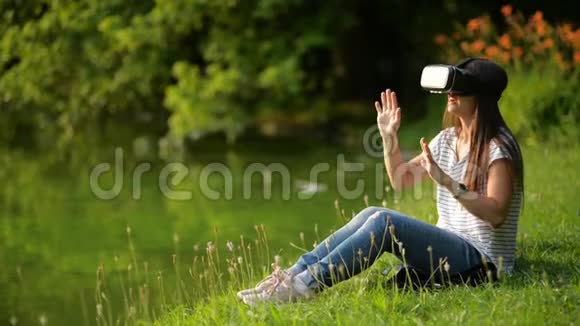 虚拟现实护目镜的年轻女子坐在城市公园的湖边布鲁内特使用头装视频的预览图