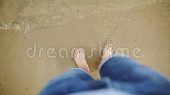人脚被海浪冲走把它们埋在沙子里穿着蓝色牛仔裤的白种人把水从脚上刷下来视频的预览图