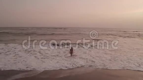 日落时分美丽的比基尼女郎在黑色海滩上的鸟瞰视频的预览图