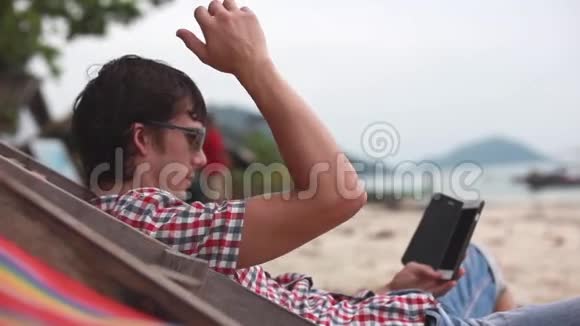 户外戴墨镜的商人躺在日光浴床上在海边看手机上的东西1920x1080视频的预览图