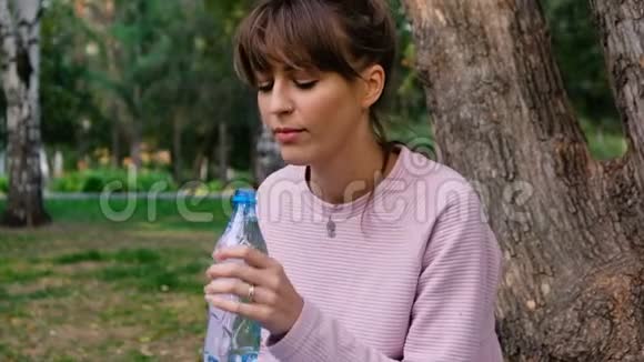 迷人的金发女孩在户外愉快地喝水一个年轻的女人正在从塑料里喝干净的水视频的预览图