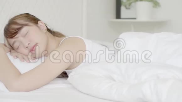 美丽的亚洲年轻女子躺在床上头靠在枕头上舒适而快乐地躺在卧室里移动着平底相机视频的预览图