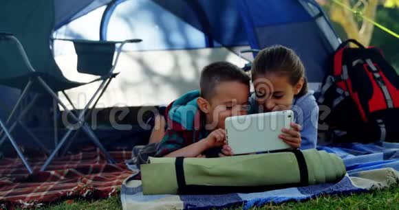 在营地帐篷外使用数字平板电脑的小兄弟视频的预览图