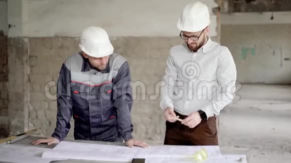 两名戴防护头盔的工程师在施工区域一起工作站在大楼里的督察和领班视频的预览图