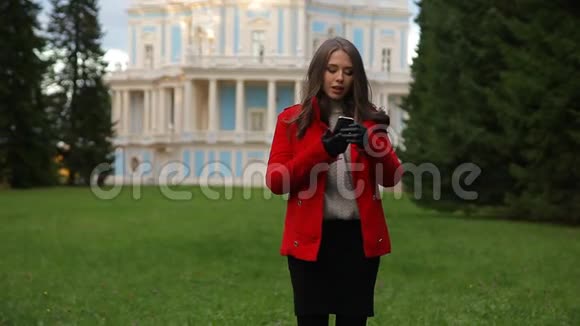 穿着红色外套的白种人女人在智能手机上说话走路视频的预览图