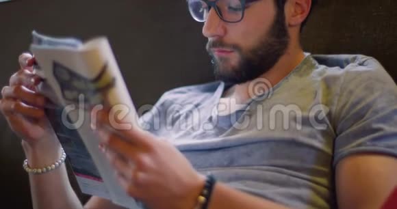 你g千禧一代男子在家中休闲着装放松阅读杂志报纸4k视频视频的预览图