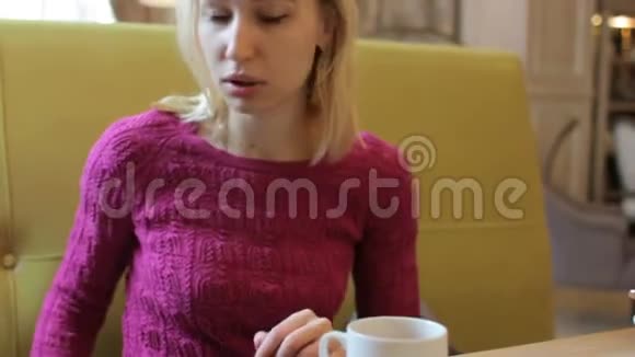 年轻漂亮的金发女人在咖啡馆里用手机打电话喝咖啡视频的预览图