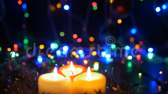 三个新年蜡烛特写和新年花环有彩色灯光的模糊背景视频的预览图