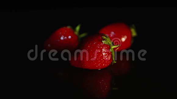 三个草莓躺在黑暗的桌子上黑色的背景在灯光下视频的预览图