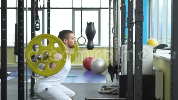 健身房的力量训练用杠铃做蹲的家伙健美运动员用杠铃做运动侧视视频的预览图