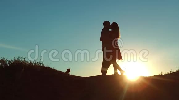 情侣在夕阳下剪影亲吻拥抱慢动作视频年轻夫妇在日落时接吻男人和女孩见面视频的预览图