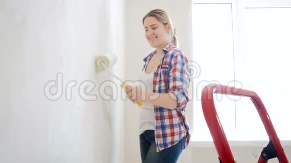 4K镜头美丽的微笑女人在新家用滚筒画墙视频的预览图