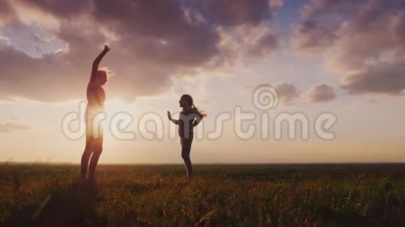 年轻的女人和她的女儿在日落时做运动他们站在风景如画的地方健康的家庭4慢视频的预览图