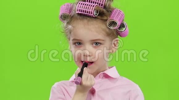 穿着粉红色卷发的孩子看着镜子用红色的口红嘴唇画画绿色屏幕快关门慢动作视频的预览图