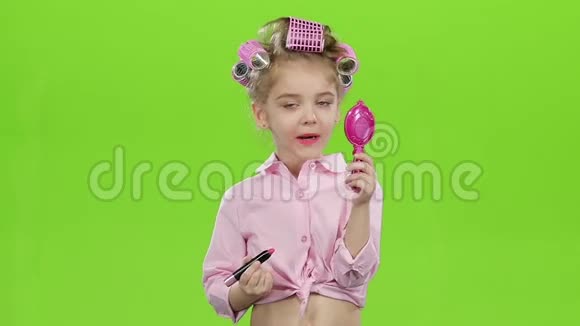 卷发器里的孩子手里拿着一面镜子用口红涂口红绿色屏幕慢动作视频的预览图