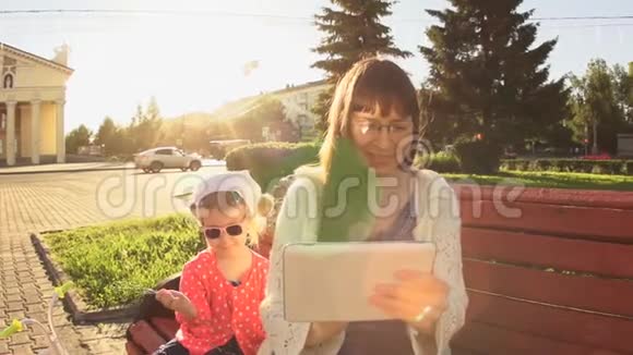 日落时分妈妈和女儿正坐在路边的一个广场上的长凳上视频的预览图