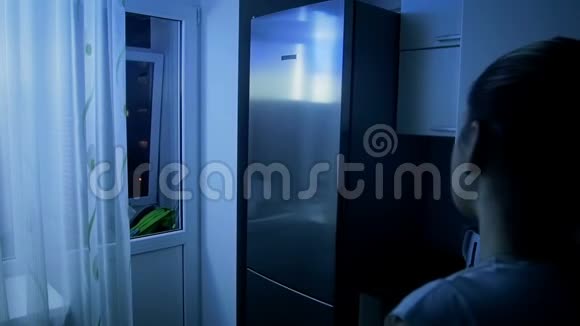 年轻女子晚上从冰箱里拿苹果的慢镜头视频的预览图