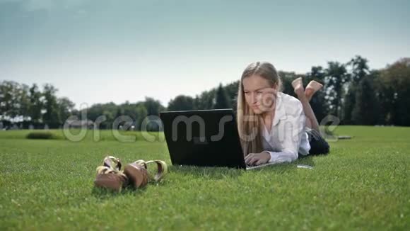 女商人拿着笔记本电脑躺在草地上视频的预览图