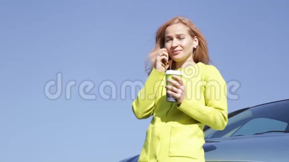 自信的年轻商务女性在她的车附近喝咖啡正在打手机视频的预览图