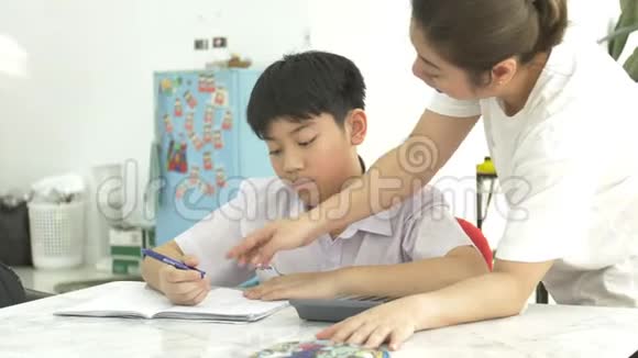 亚洲母亲的慢动作帮助她的儿子在白色桌子上做作业视频的预览图